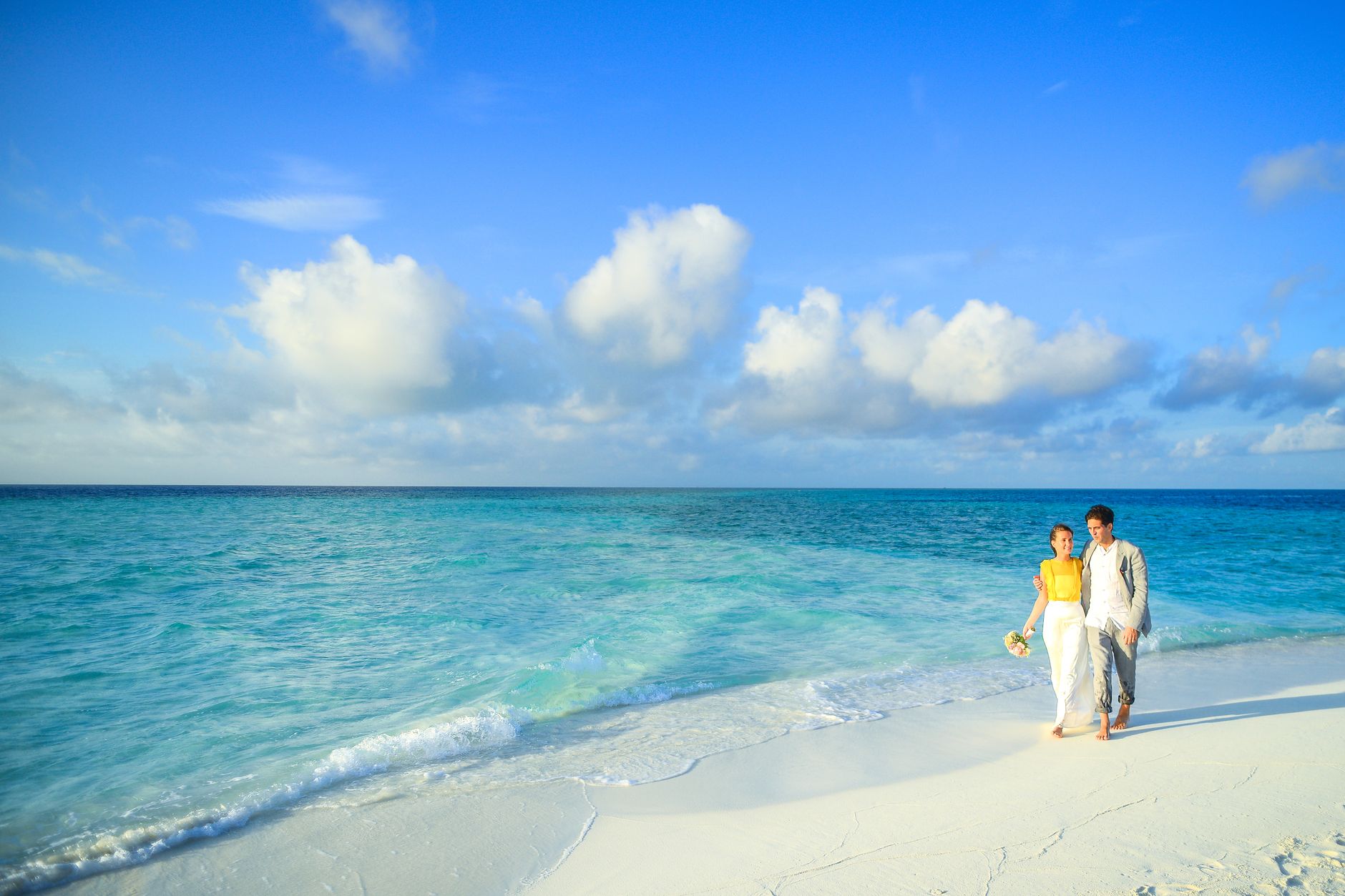 A couple enjoys a romantic stroll along a pristine tropical beach with turquoise waters.