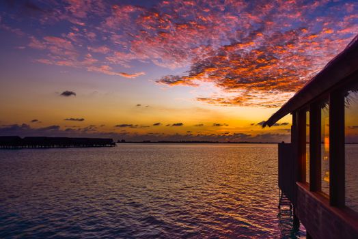 Capture the serene beauty of a tropical sunset with vibrant colors reflected on the ocean's surface.
