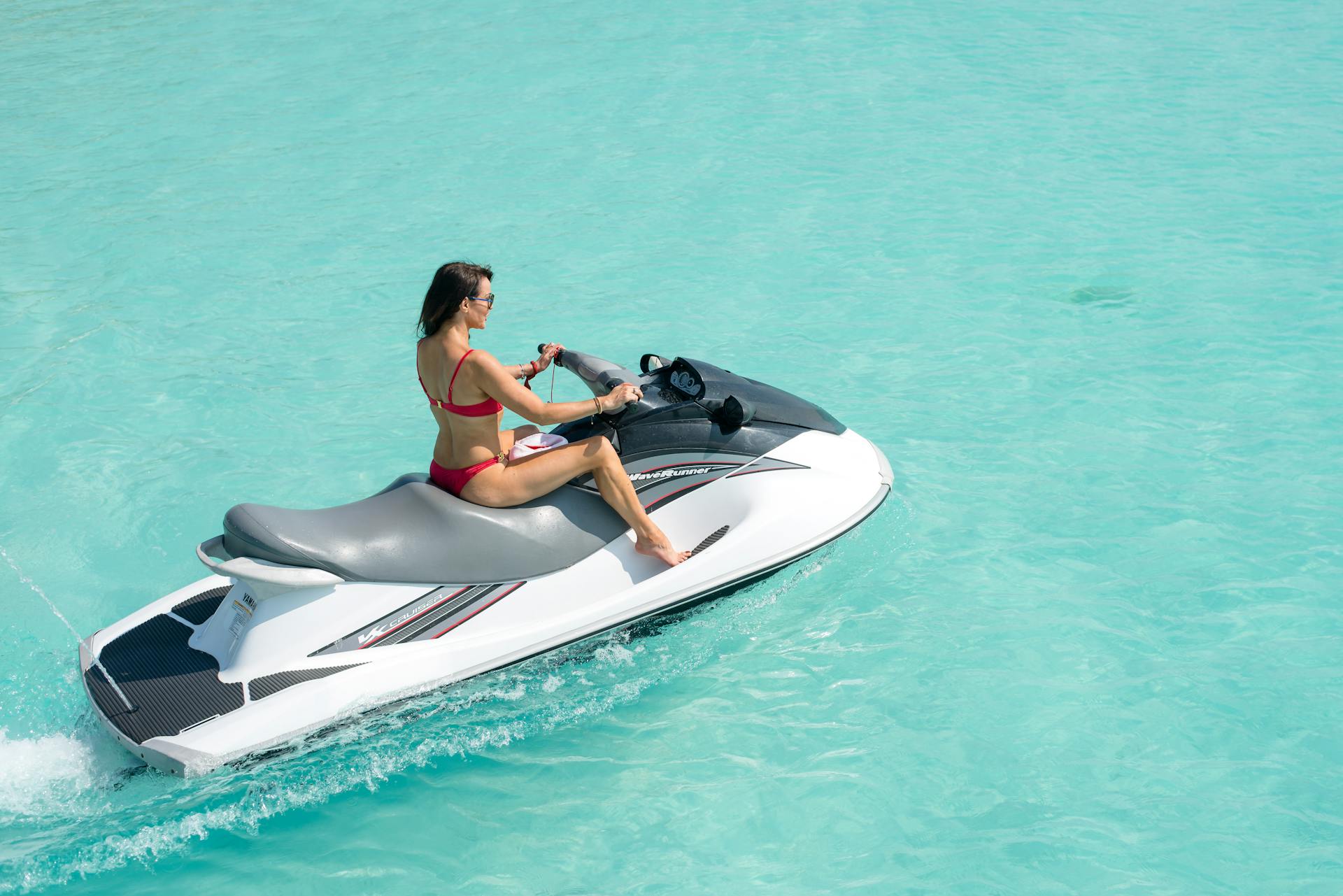 A woman enjoys a sunny day riding a jet ski on clear turquoise waters. Perfect for travel or beach themes.