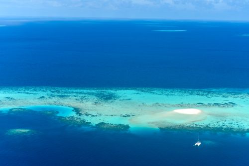 Free A stunning aerial view of a tropical island surrounded by turquoise waters and coral reefs. Stock Photo