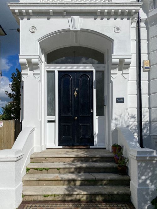 Free Classic Victorian entrance with black door and white facade, sunlight casting shadows. Stock Photo