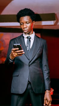 A young businessman in a suit checks his smartphone indoors, exuding style and confidence.
