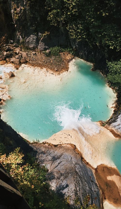 Free A breathtaking aerial view of turquoise waters cascading into a rocky pool surrounded by lush forest. Stock Photo