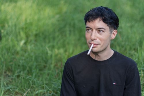 Free Young man with short hair smoking in a green outdoor setting. Stock Photo