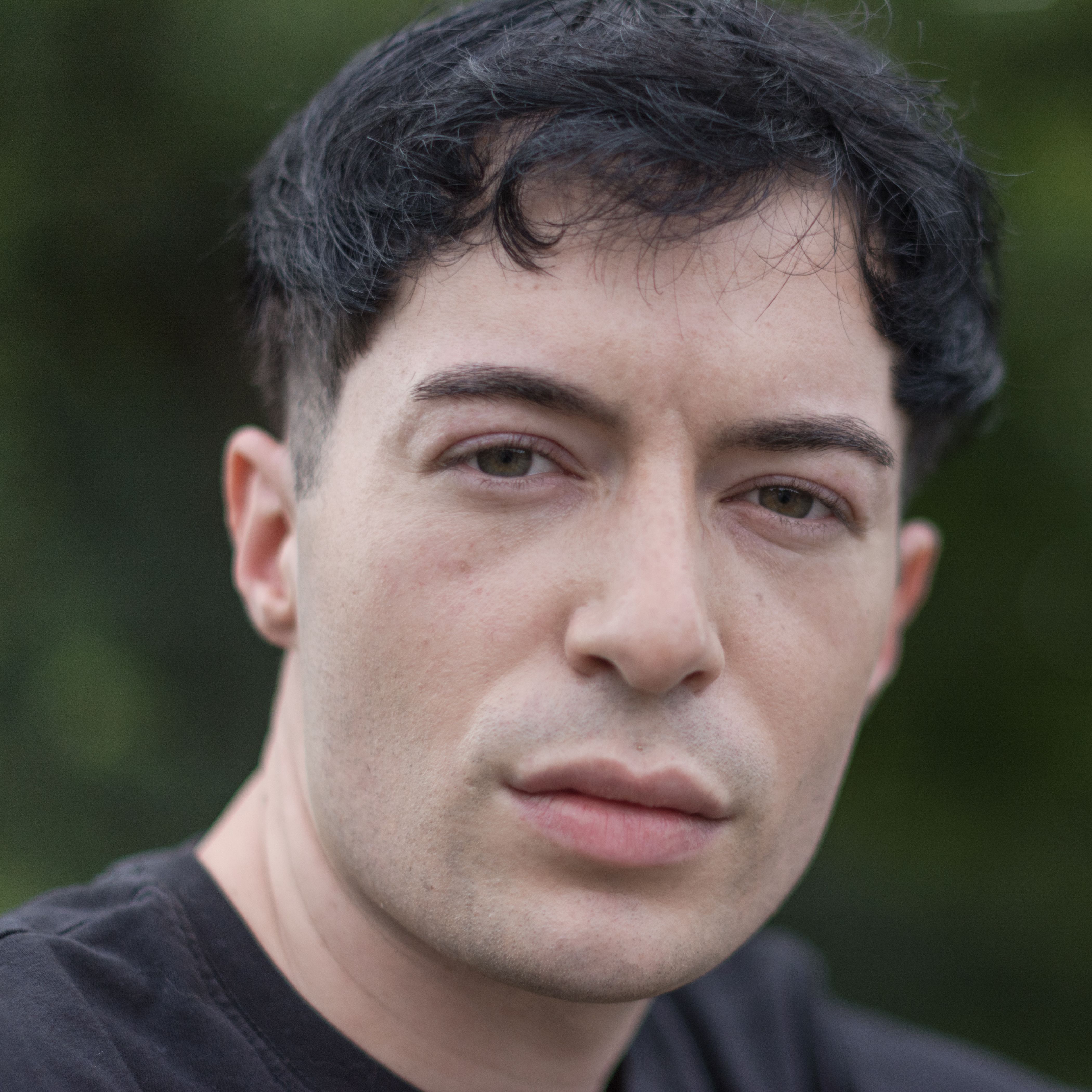 Intimate close-up portrait of a man with neutral expression outdoors.