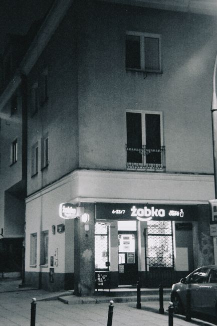 Wnętrze typowego sklepu Żabka z widocznymi różnymi produktami na półkach, z sylwetką uśmiechniętego ajenta lub sprzedawcy za ladą, symbolizującego lokalną autonomię w asortymencie.