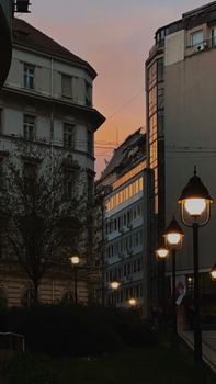 Street scene in Belgrade with lit lamps, historic buildings, and a vibrant sunset sky.