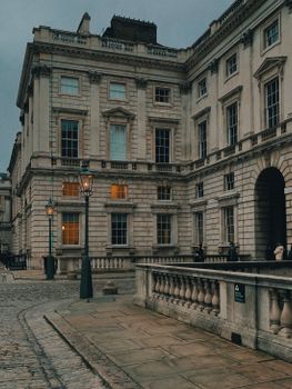 Stone architecture of Somerset House in London's moody twilight ambiance with vintage street lamps.