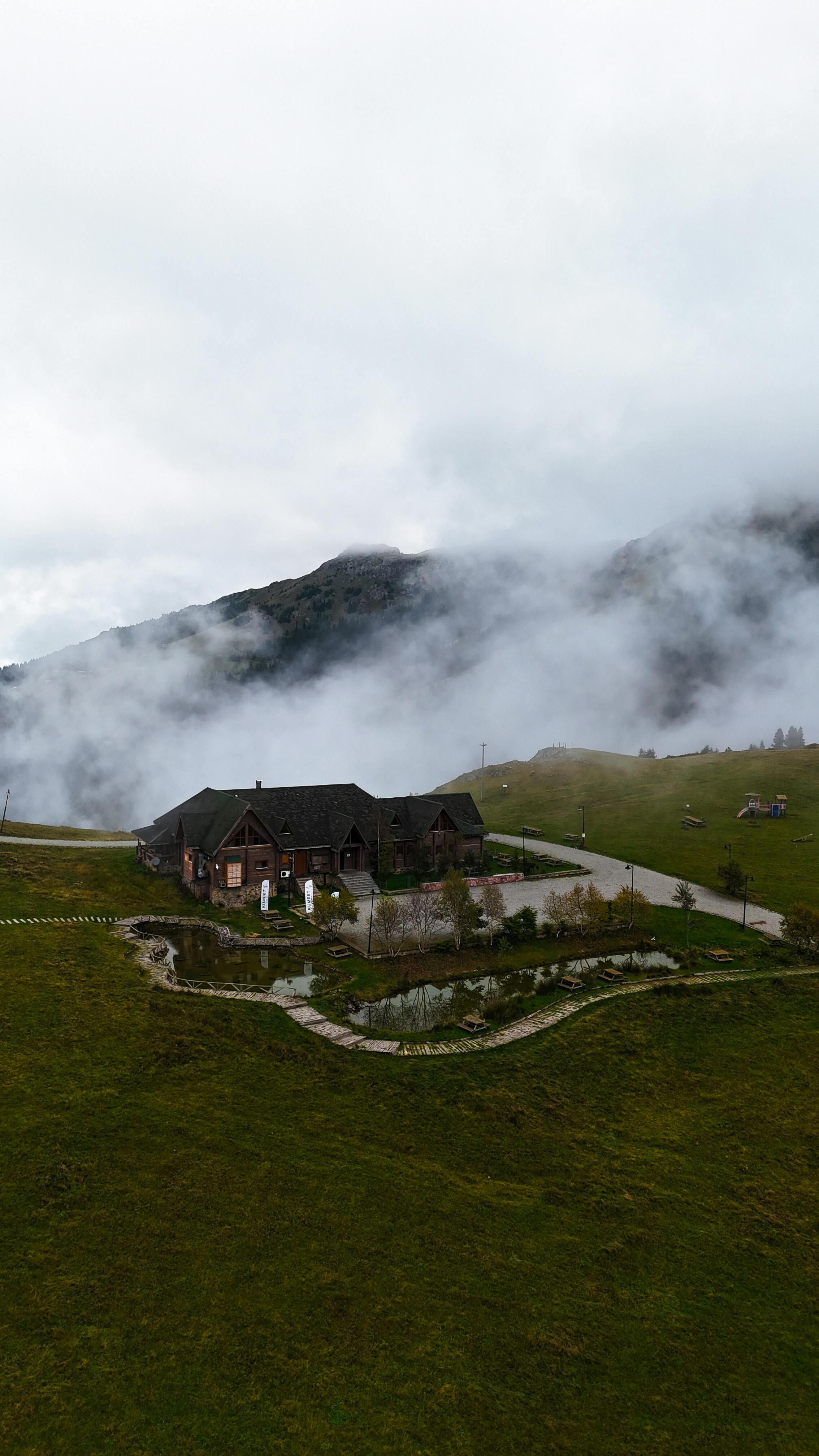 Scenic view of a house amidst misty mountains and rolling hills.