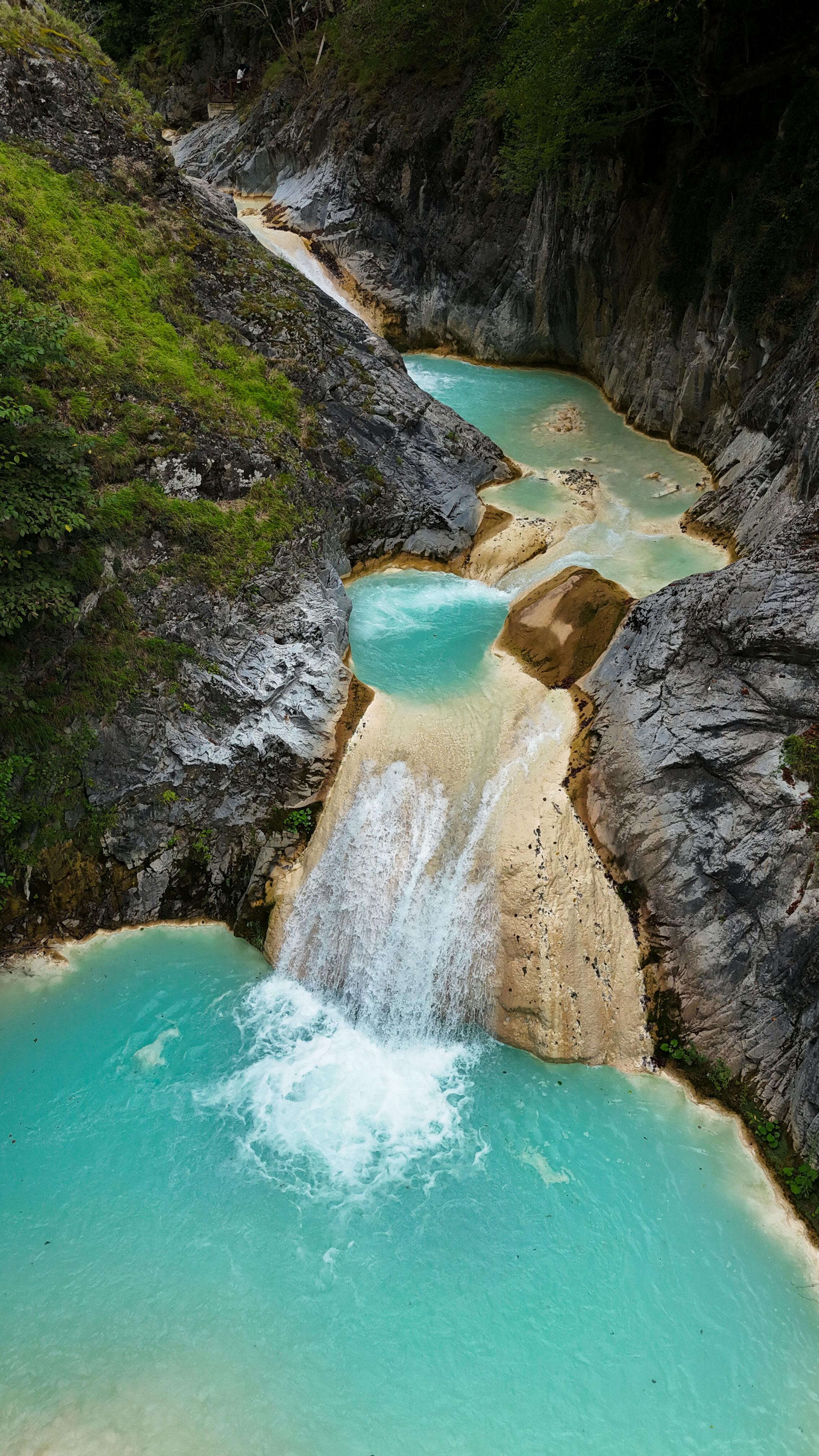 A breathtaking view of a turquoise waterfall cascading through a rocky gorge surrounded by lush greenery.