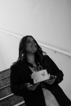 Smiling woman holding birthday cake on stairs, joyful moment.