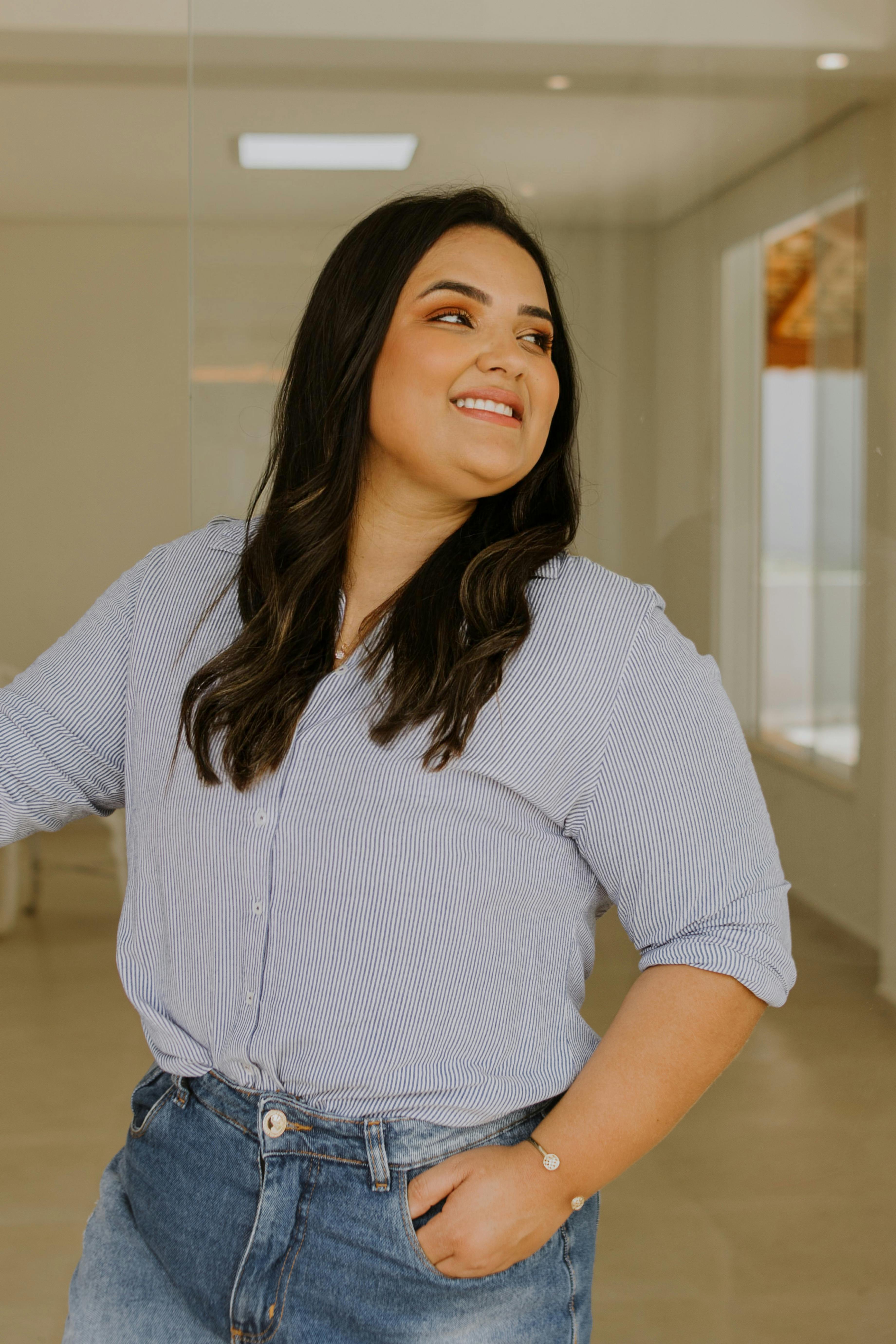 Smiling woman in casual attire standing confidently indoors with natural light.
