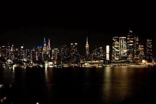 Stunning nighttime view of New York City's illuminated skyline reflecting on the water, featuring iconic landmarks.