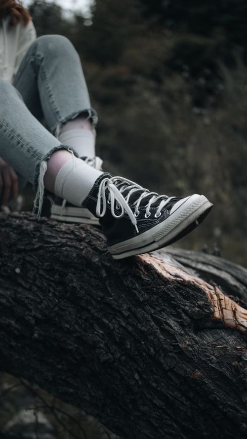 Free A young woman in jeans and sneakers sits relaxed on a tree branch, capturing fall's essence. Stock Photo
