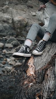 Teenager in stylish sneakers relaxing outdoors on a tree stump during fall in Merzifon, Türkiye.
