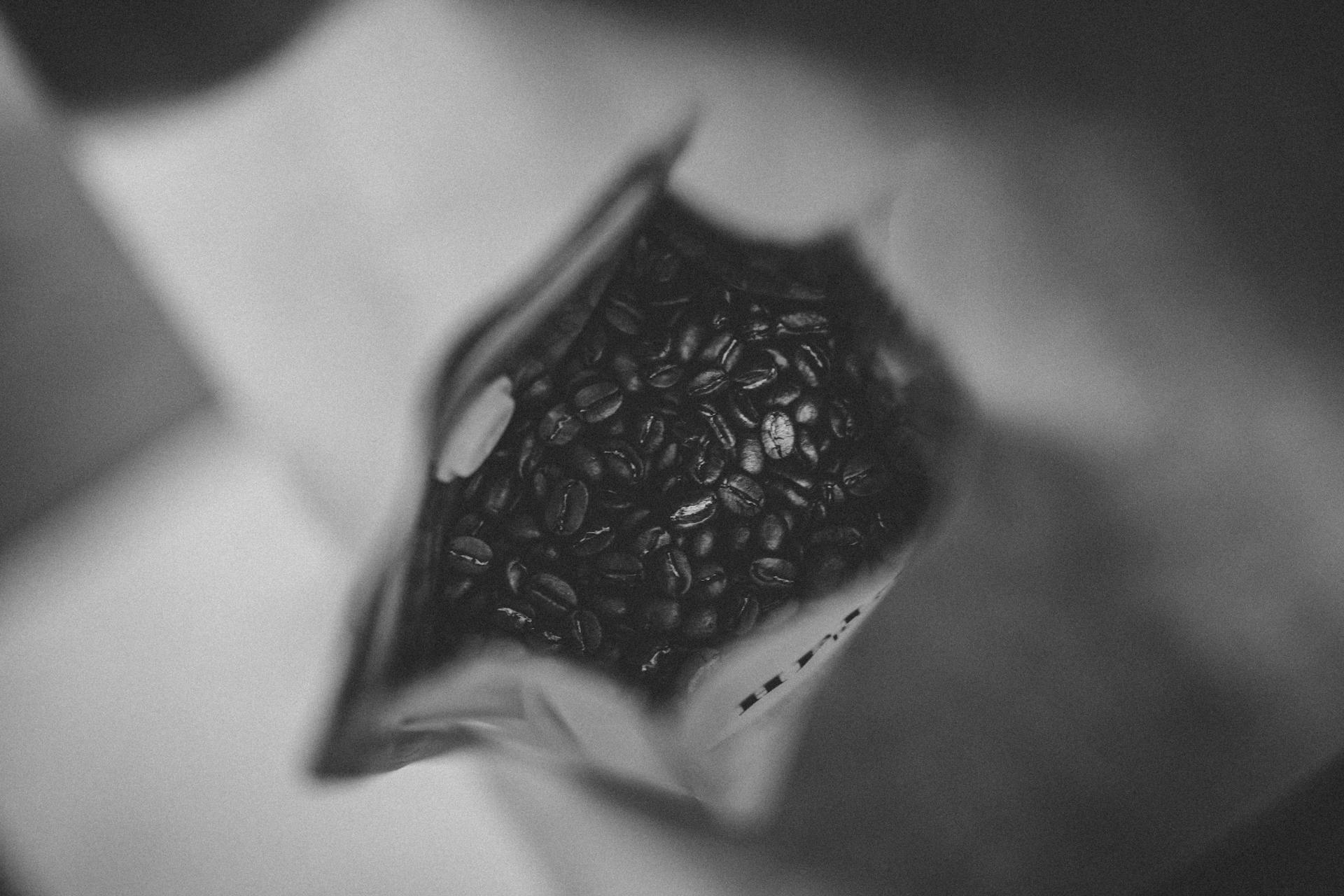 Black and white image capturing coffee beans in a bag from above, providing a moody artistic look.