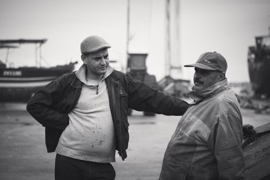 Two fishermen sharing a moment at Tabarka harbor in Tunisia, captured in black and white.