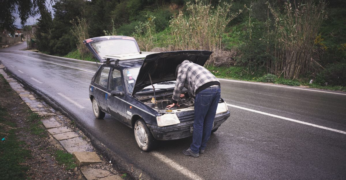 An individual repairing a car on a rainy road in Tabarka, showcasing urgent roadside vehicle maintenance.