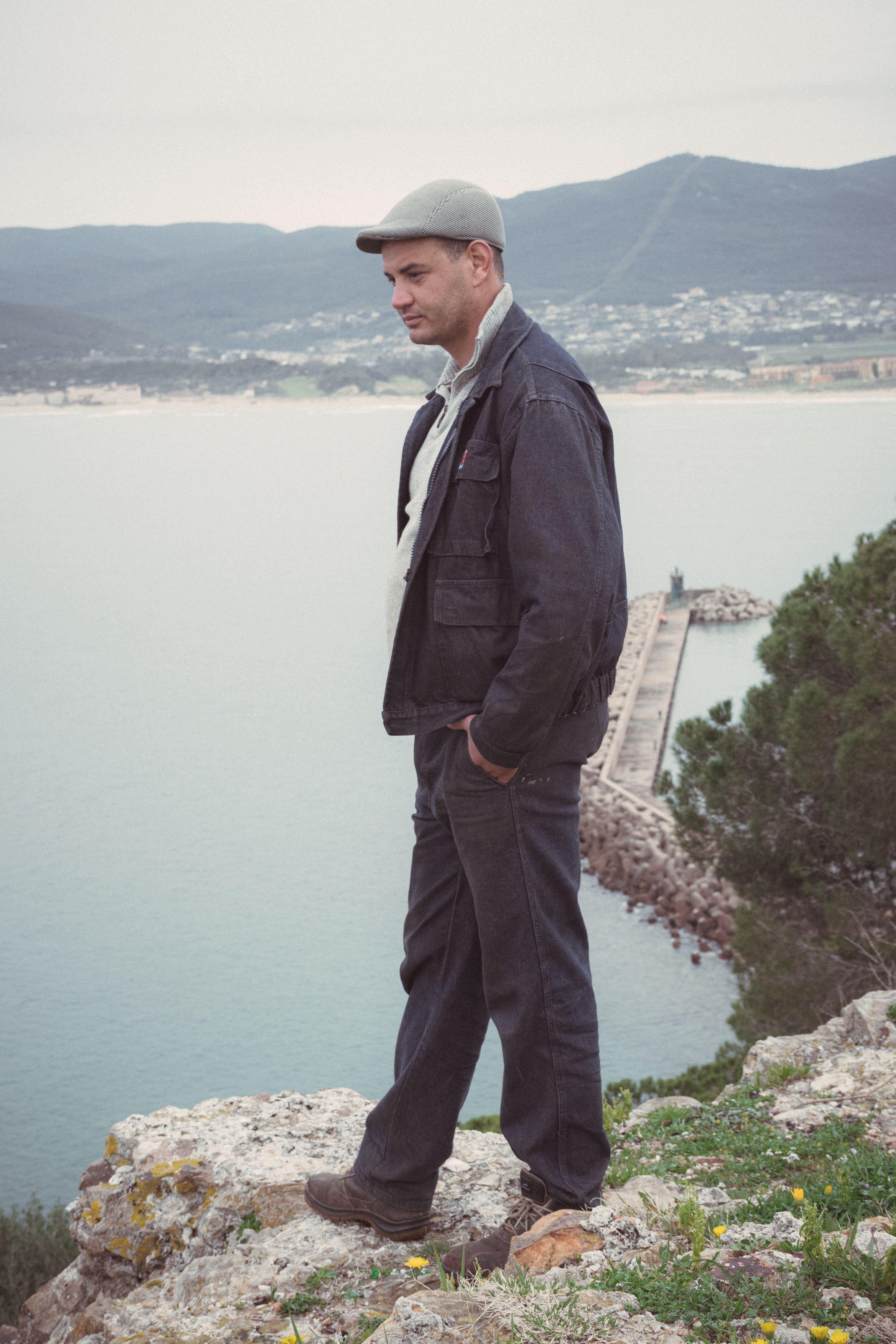 Man standing on cliffside in Tabarka, Tunisia, with scenic coastal view.