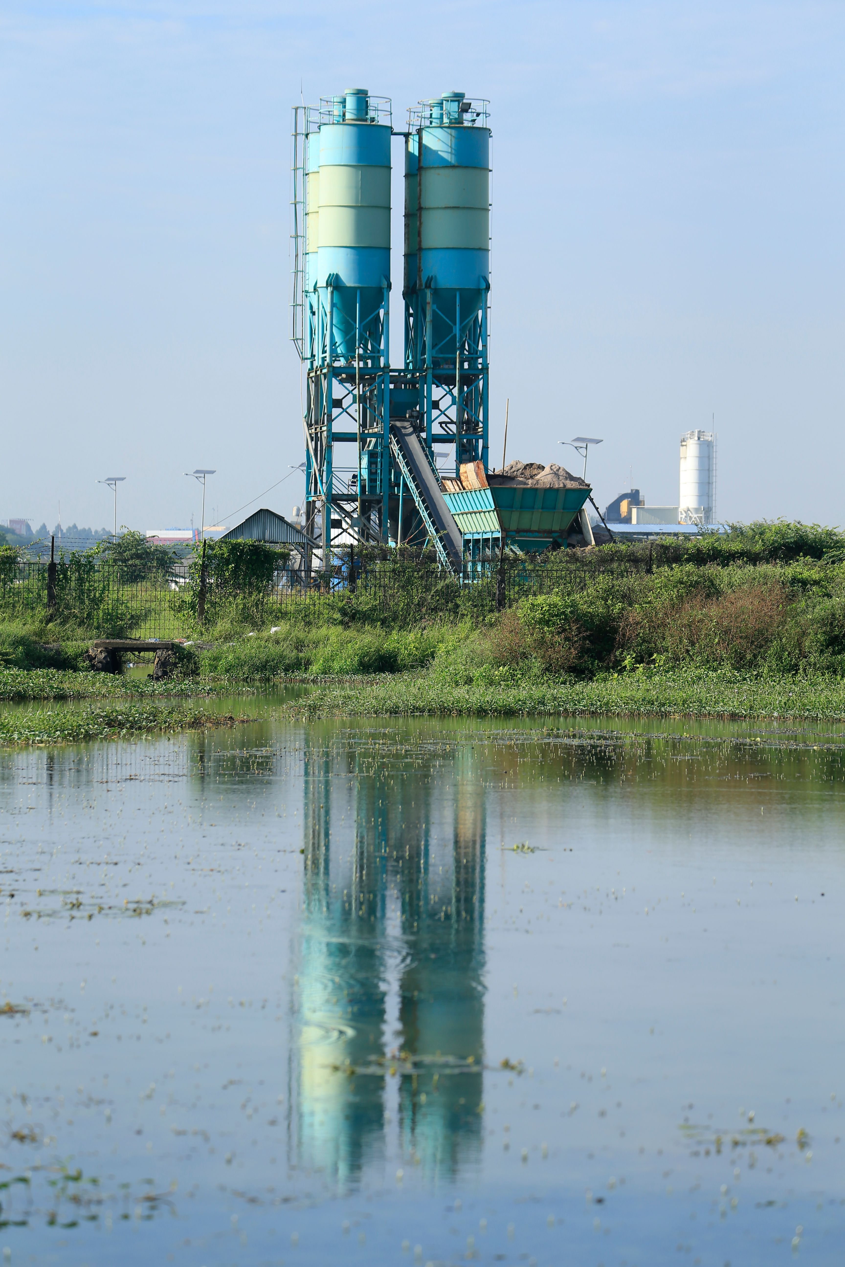 Industrial cement silos reflecting in water · Free Stock Photo