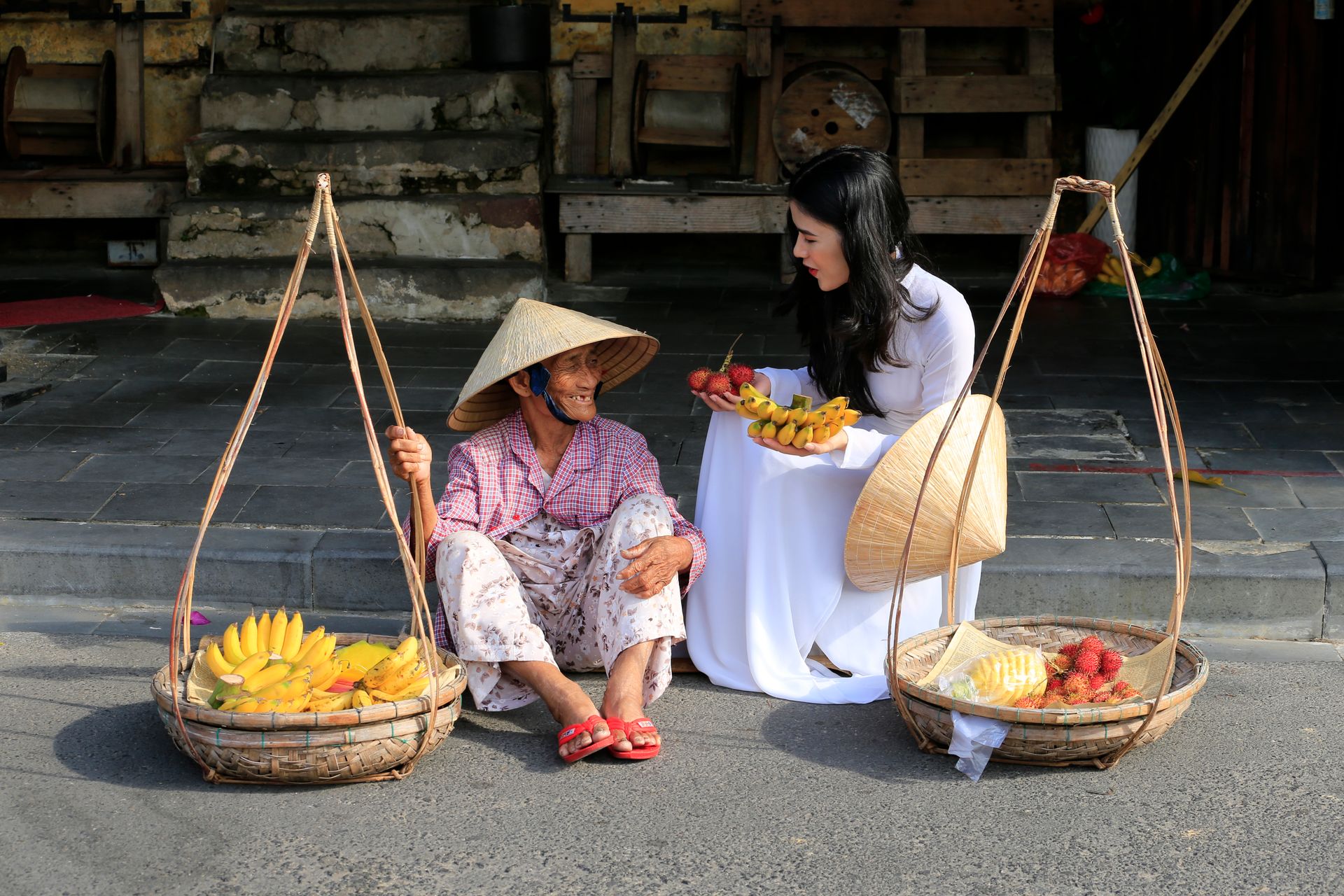 A young woman interacts with a Vietnamese street vendor selling fruits, showcasing cultural connection.