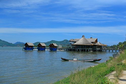Free Calm lakeside view with traditional bungalows and a pier under a clear blue sky. Stock Photo