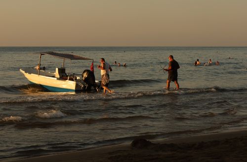 Free People enjoy a tranquil beach setting with a boat during a golden sunset. Stock Photo