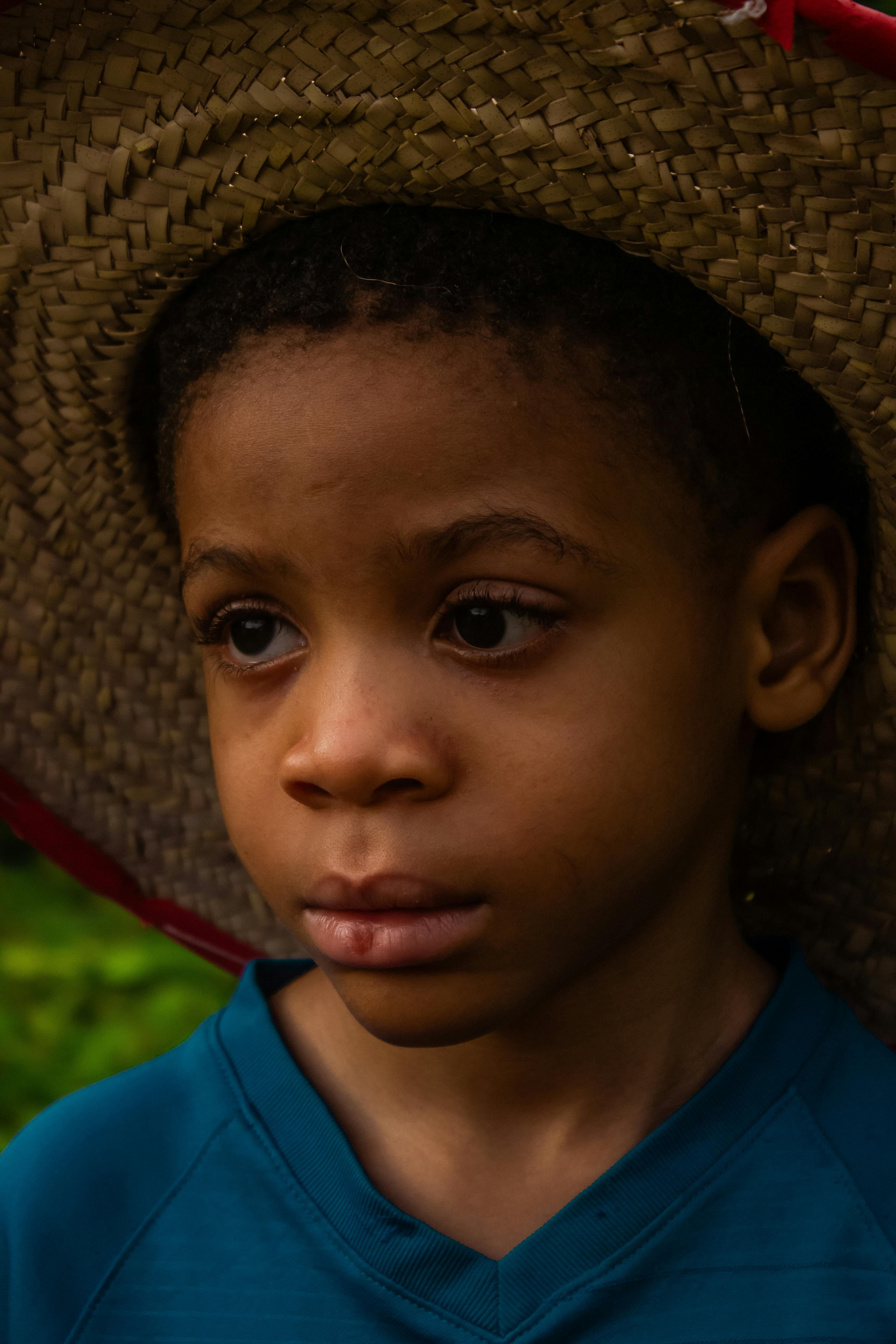 A young child with a contemplative expression wearing a straw hat, captured outdoors.