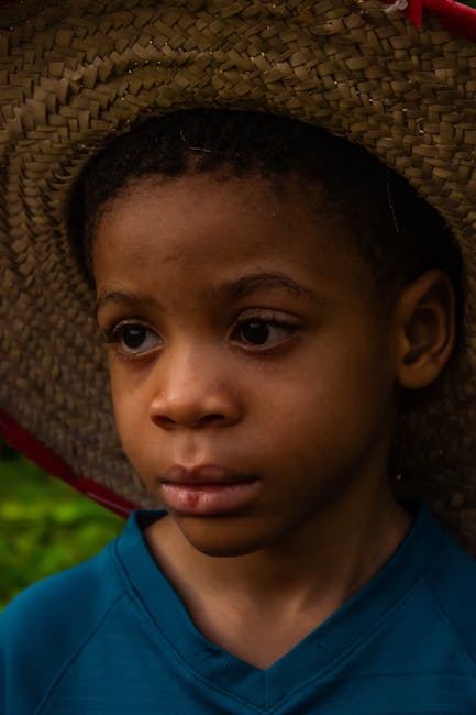 A young child with a contemplative expression wearing a straw hat, captured outdoors.
