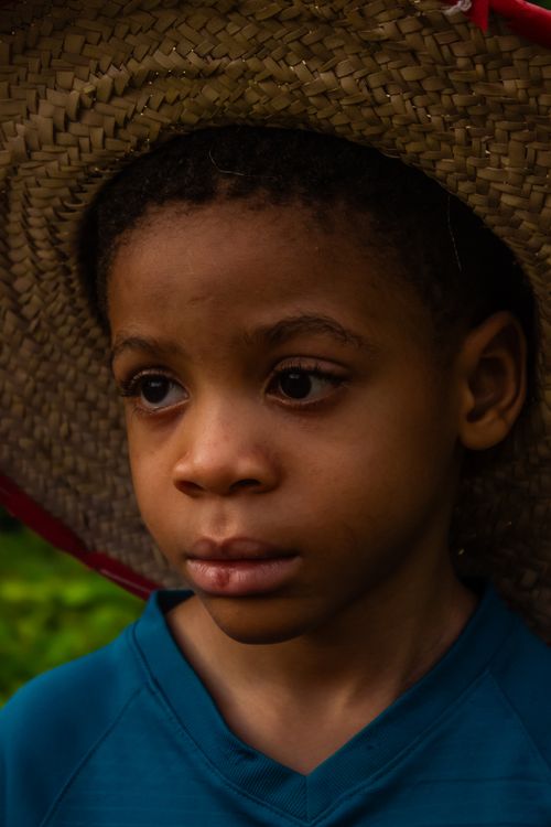 Free A young child with a contemplative expression wearing a straw hat, captured outdoors. Stock Photo