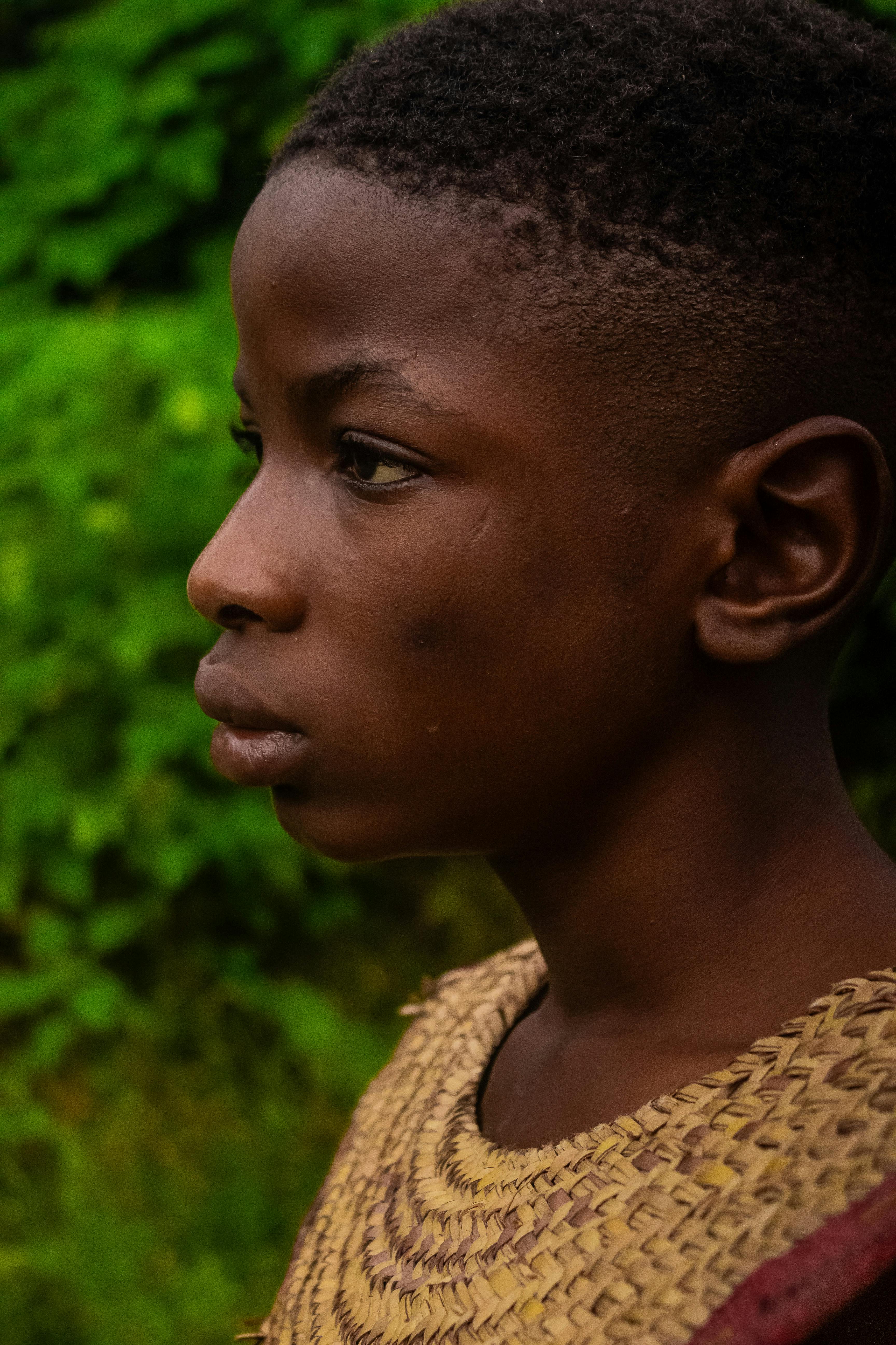 Side profile portrait of a young boy with an intense expression against a lush green background.