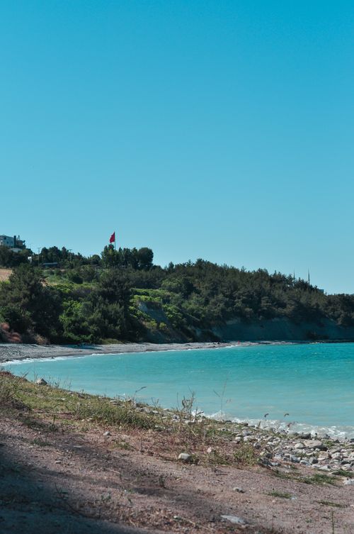 Free Tranquil beach scene with clear blue water and lush greenery under a bright sky. Stock Photo
