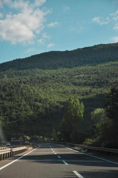 Free Sunlit highway with lush green mountain scenery under a clear blue sky. Stock Photo