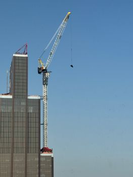 Tower crane operating on a high-rise building against a clear blue sky.