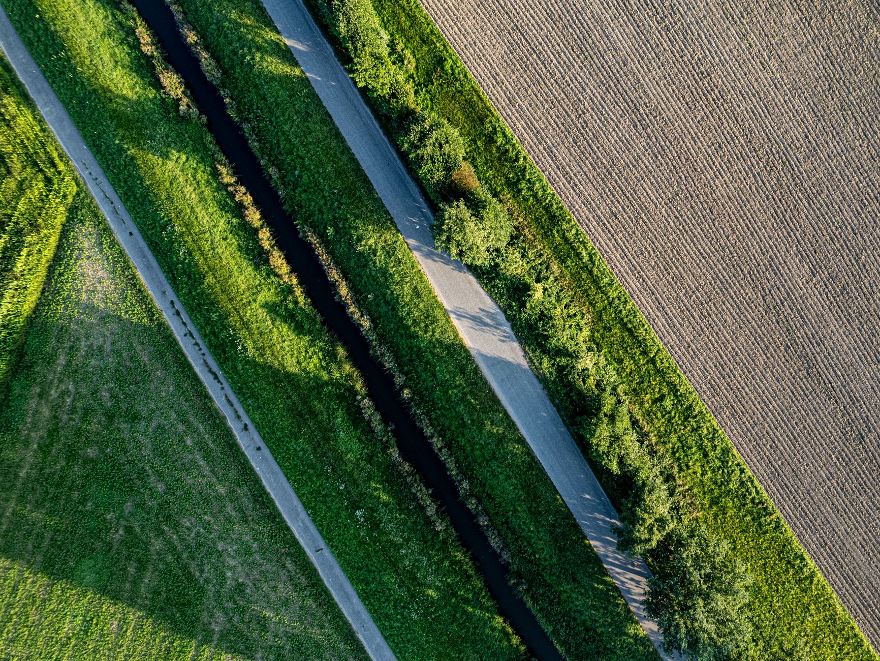 Drone shot of a canal with lush greenery and shadows in summer fields.