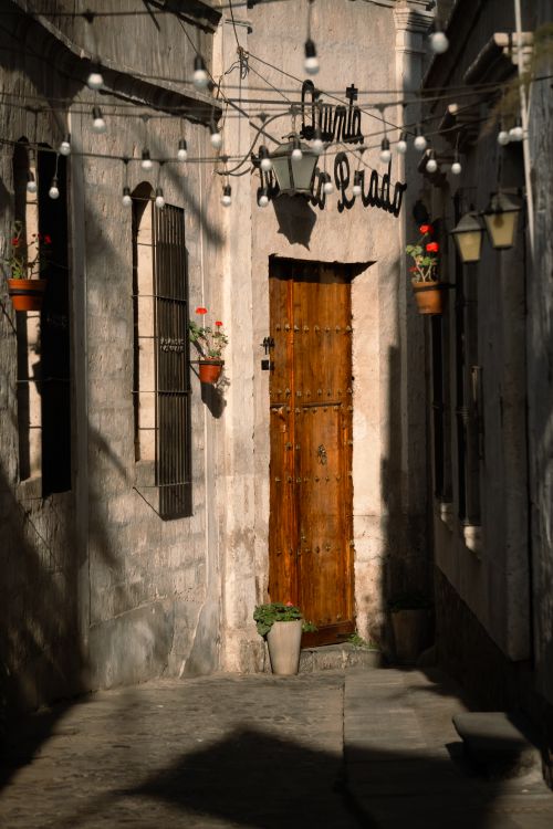 Free Sunlit rustic alley with wooden door and hanging lights, evoking vintage charm. Stock Photo