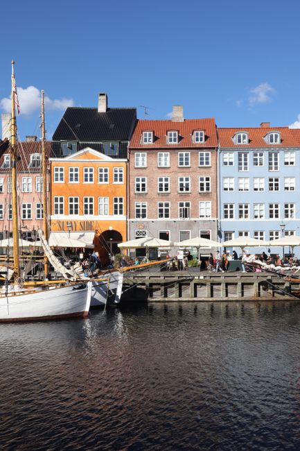 Colorful houses line the Nyhavn canal in Copenhagen with boats and people enjoying the day.