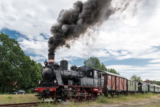 Vintage steam train with billowing smoke traveling through Geesthacht, Germany.