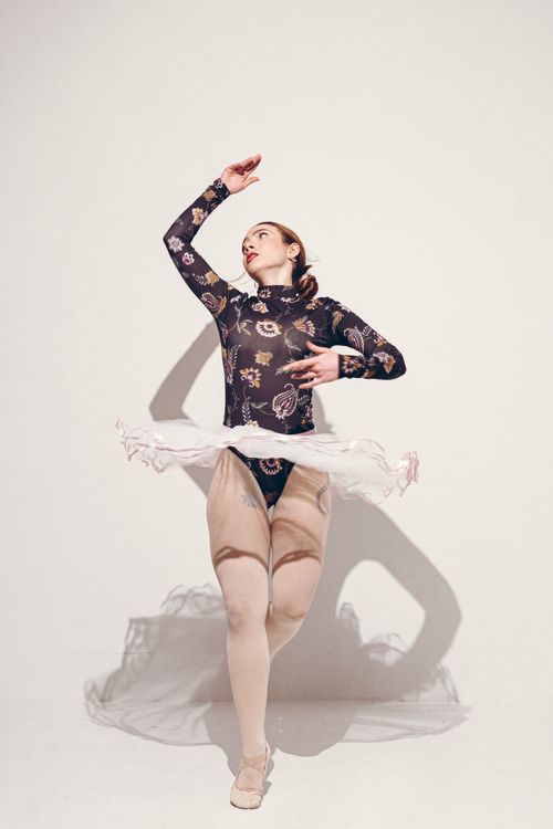 Free A redheaded ballerina in a floral outfit dances gracefully against a plain backdrop. Stock Photo