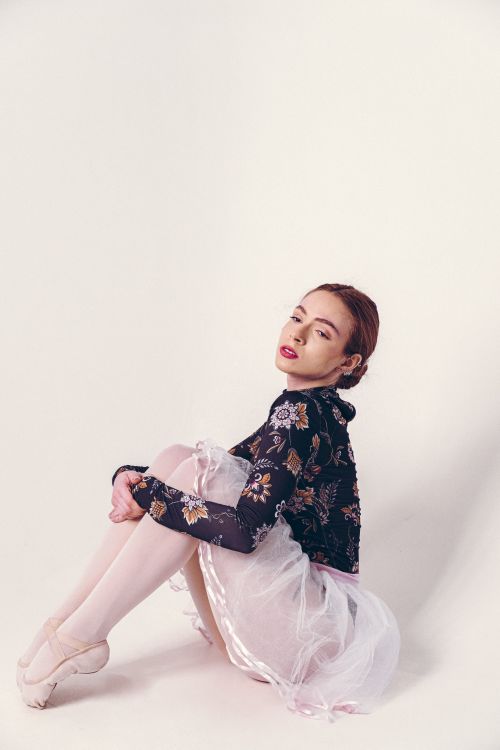 Free A young ballerina in elegant floral attire poses gracefully against a plain backdrop. Stock Photo