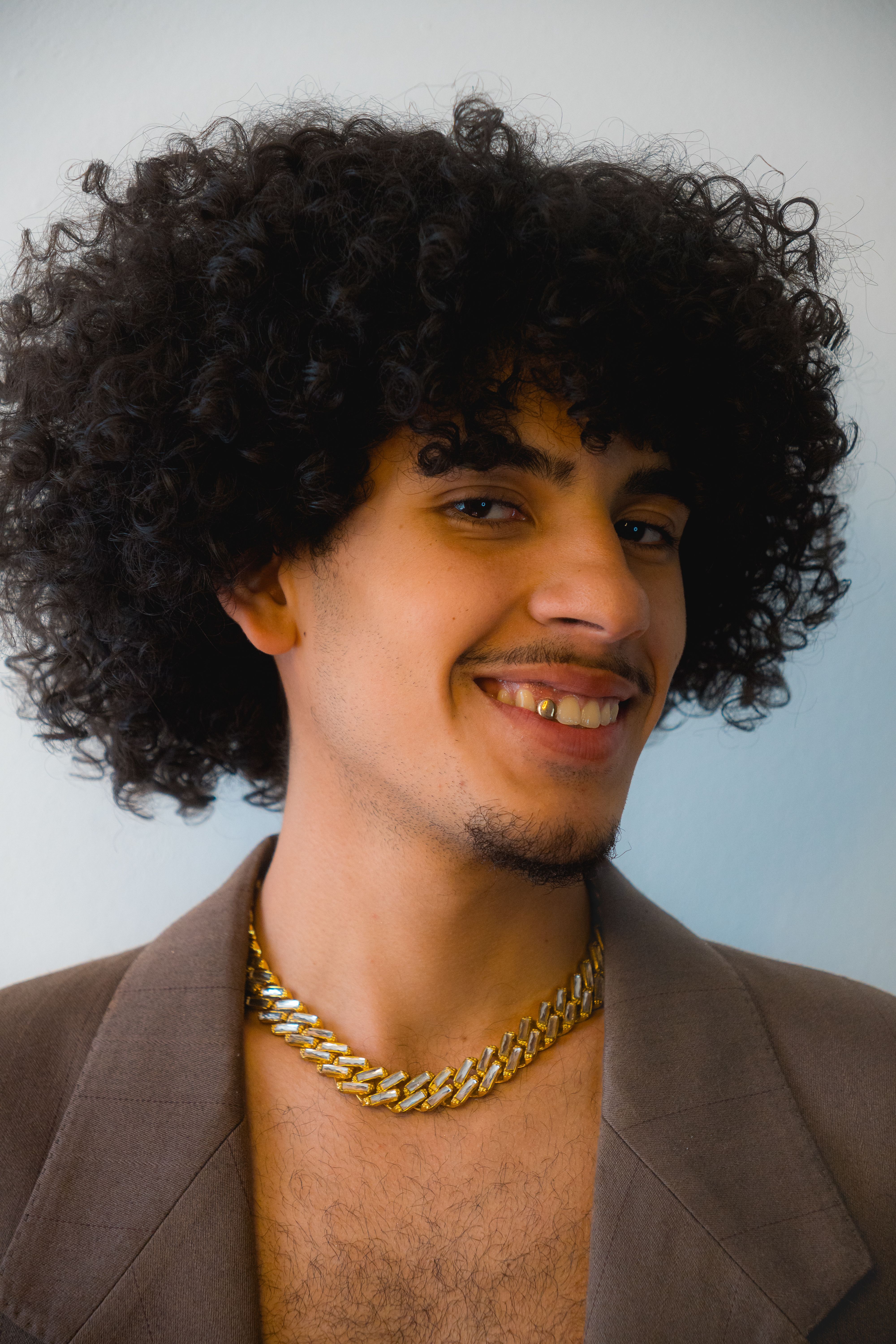 Portrait of a Young Man with Curly Hair and Jewelry · Free Stock Photo