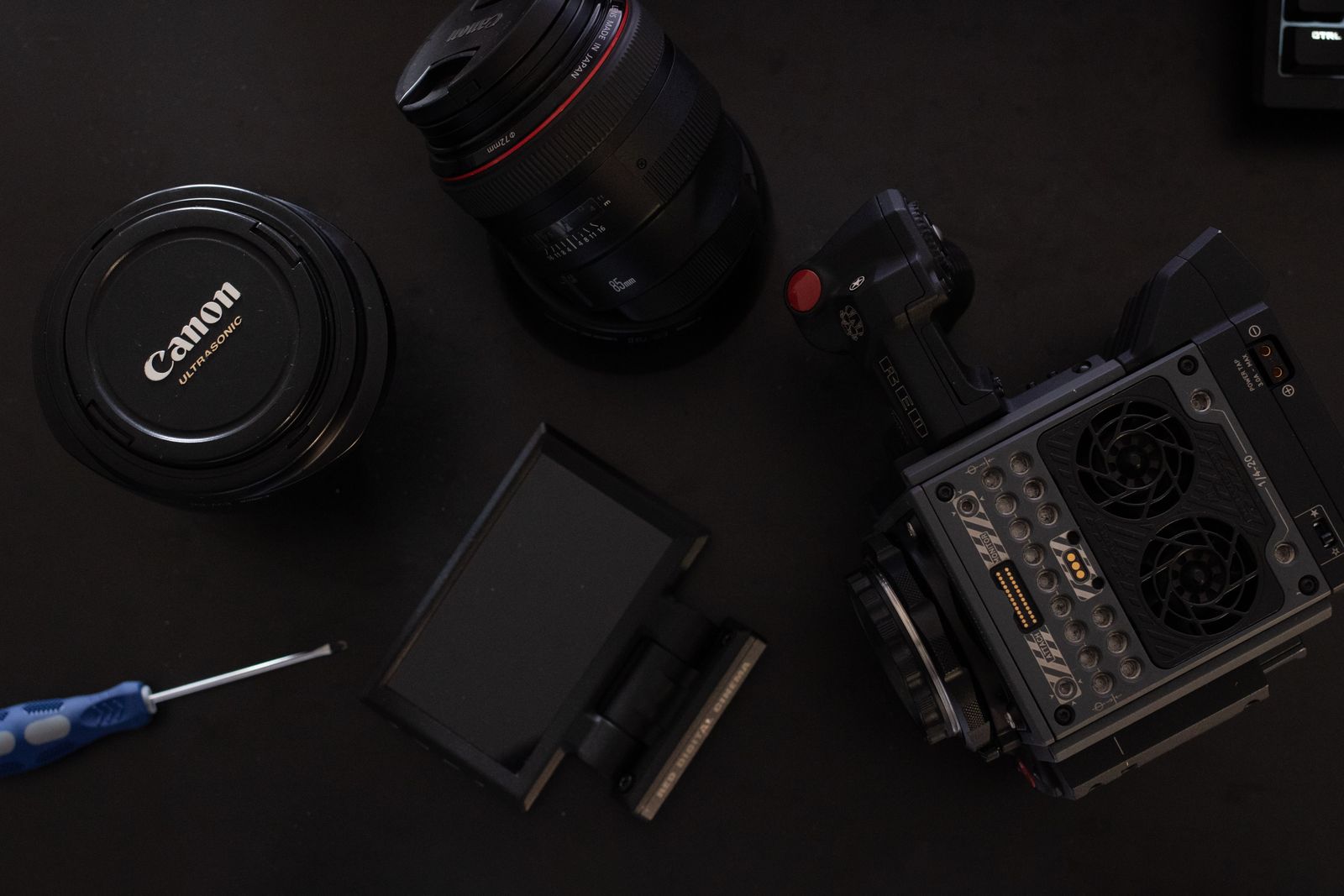 Camera body, lens, monitor, tools, and camera parts arranged on a dark work surface