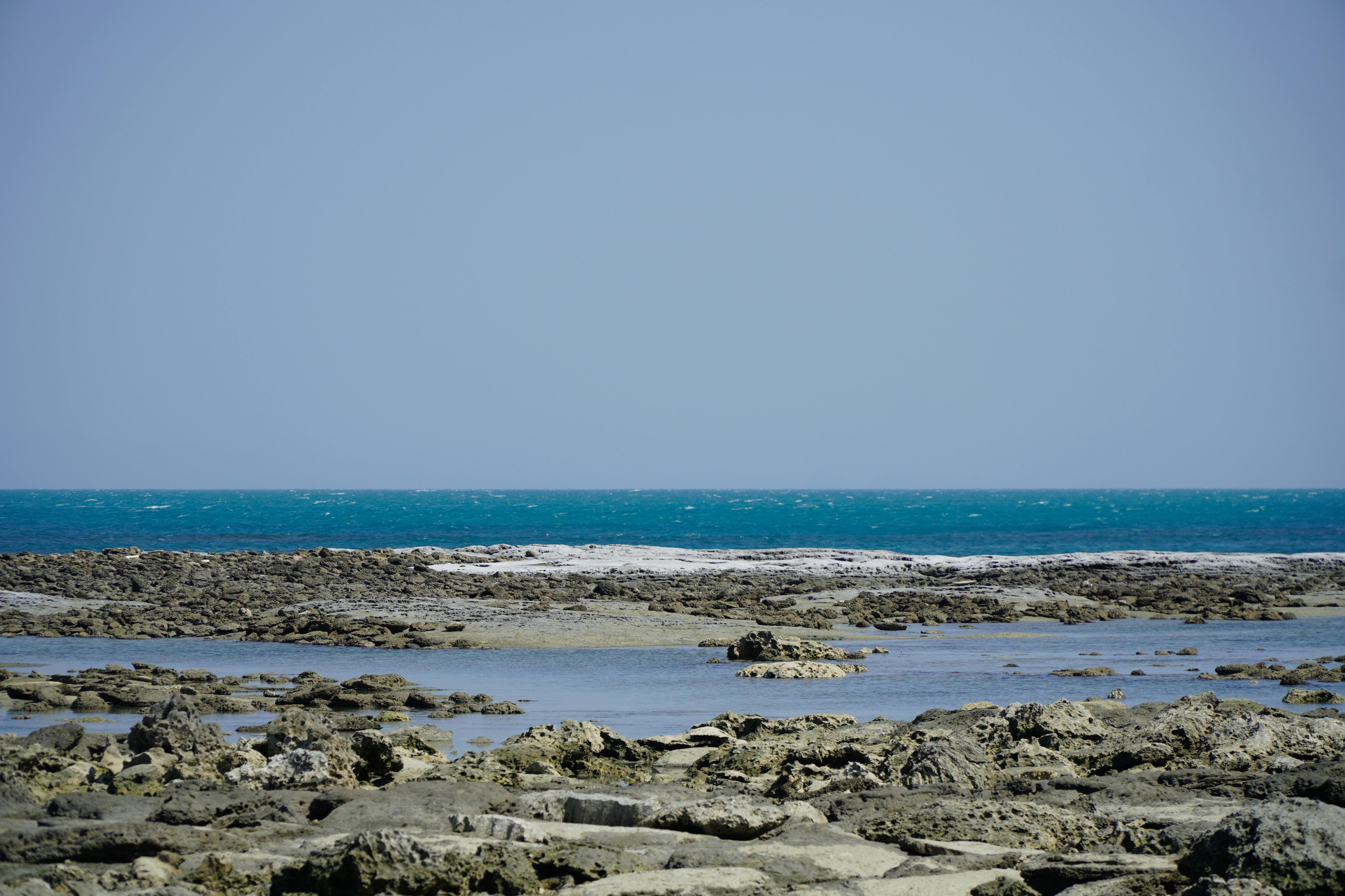 A tranquil rocky seascape featuring clear blue waters under a clear sky.