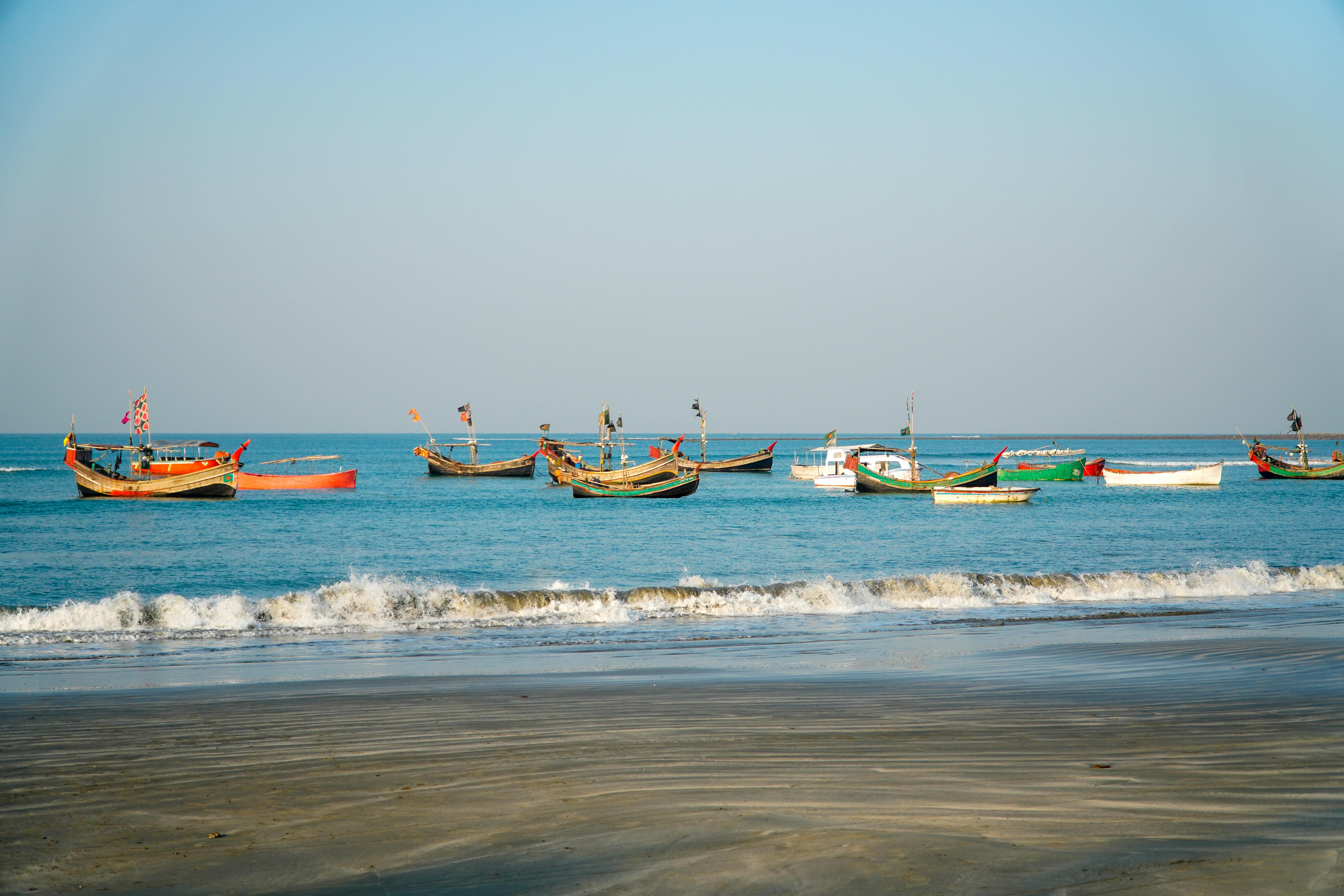 Colorful fishing boats float on calm blue waters near a peaceful tropical beach.
