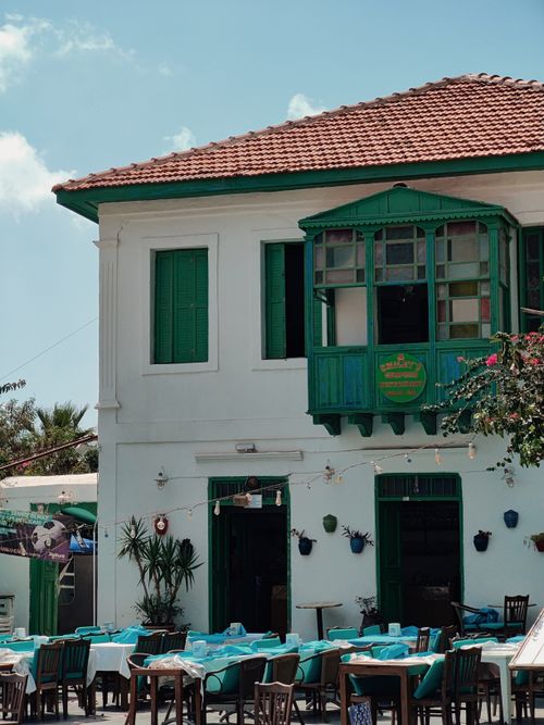 Free A quaint café with blue tables set outside a historic white building with green accents. Stock Photo
