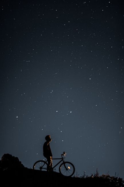 Silhouette of a person with a bicycle gazing at a star-filled night sky, evoking exploration.