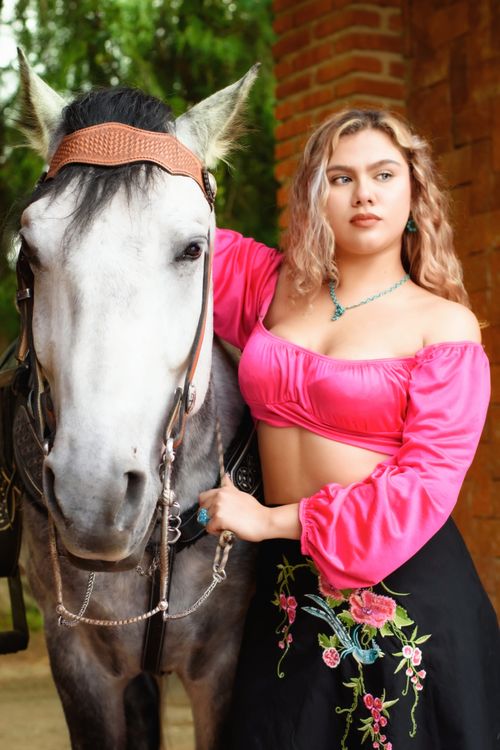 Free Young woman in vibrant attire posing beside a horse in an outdoor setting. Stock Photo