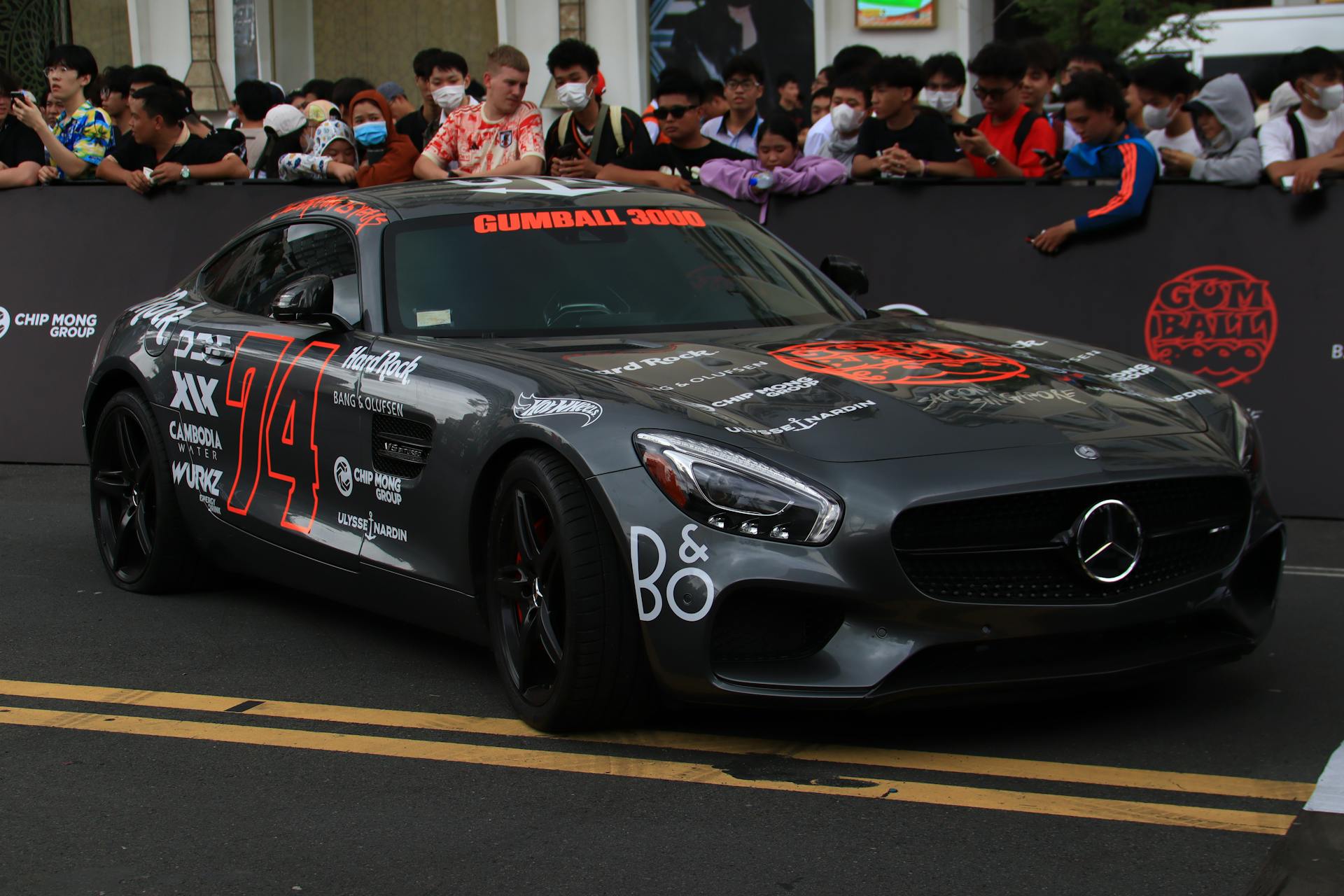 A sleek Mercedes car with sponsor decals at an event crowd backdrop.