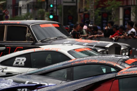Sports cars lined up at a vibrant street racing event surrounded by crowds.