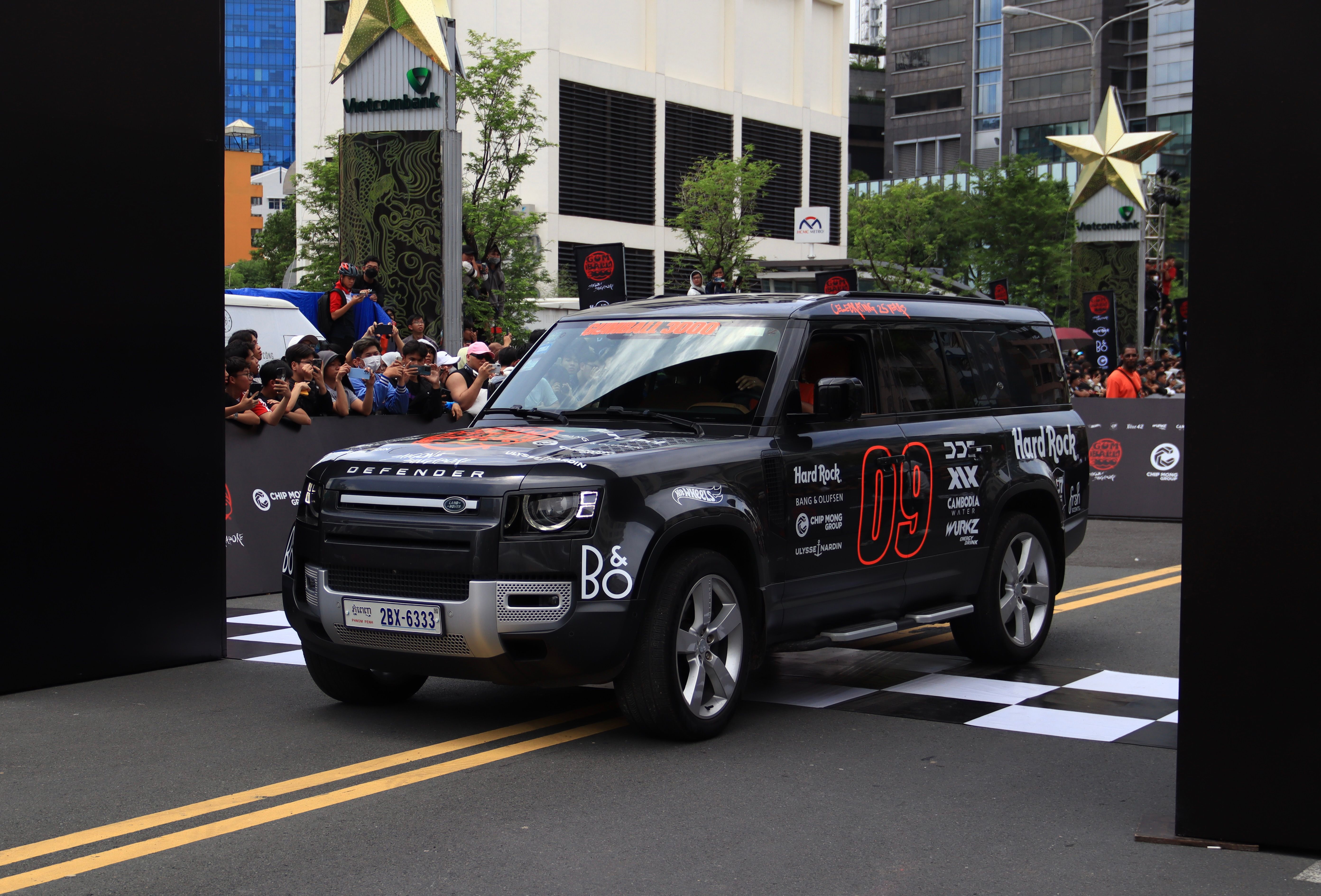 A Land Rover Defender at the starting line of a city racing event with a crowd of spectators.
